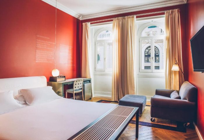 Iberostar Las Letras Gran Via gay-friendly hotel room. Pet-friendly room with red walls, large windows, bed, desk and chair. Madrid hotel.
