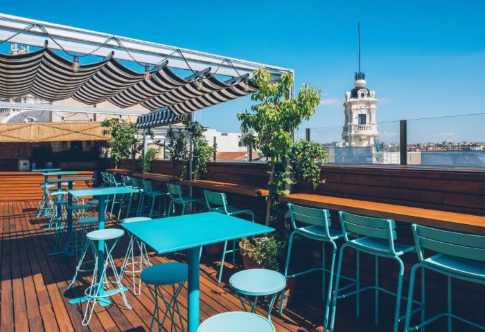 Iberostar Las Letras Gran Vía's rooftop bar. Gay-friendly, pet-friendly hotel in Madrid, Spain. Turquoise tables and chairs under a striped awning.