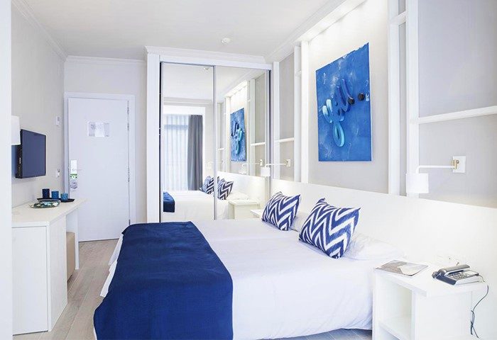 Ibersol Antemare Adults Only gay-friendly hotel room. White decor with blue accents. Double bed, mirrored closet, and modern art.