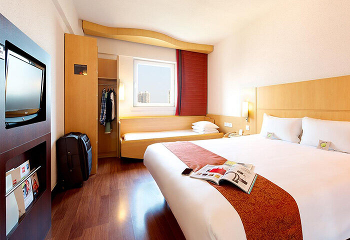 Ibis Beijing Dongdaqiao Hotel room. Gay-friendly hotel with a double bed, TV, luggage, and magazine. Comfortable stay in Beijing.