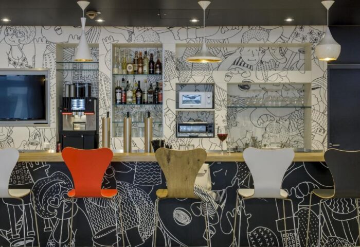 Ibis Berlin Kurfuerstendamm hotel bar. Gay-friendly hotel with quirky, modern design. Bar with stools, drinks, and black & white cartoon mural.