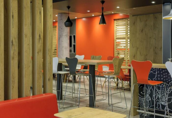 Interior of Ibis Berlin Kurfuerstendamm, a gay-friendly hotel. High tables with chairs, orange wall, and modern design. Great for gay travelers.