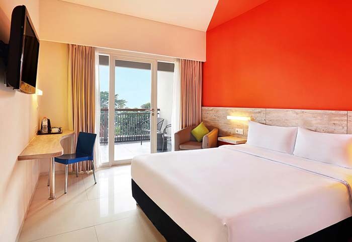Ibis Budget Bali Seminyak room. Gay-friendly hotel with balcony, bed, desk, and vibrant orange wall. Modern, clean design for gay travelers.