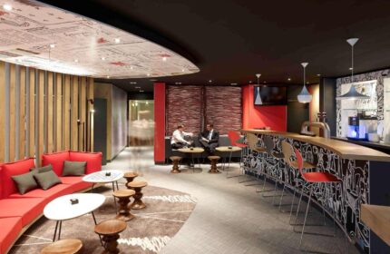 Ibis Hotel Koeln Centrum's bar area. Gay-friendly hotel with modern design, red accents, bar seating, and lounge. Perfect for Köln travel.