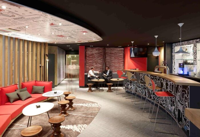 Ibis Hotel Koeln Centrum's bar area. Gay-friendly hotel with modern design, red accents, bar seating, and lounge. Perfect for Köln travel.