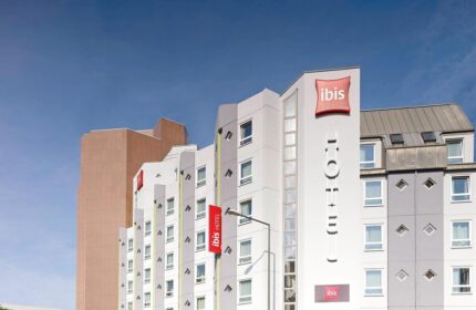 Ibis Hotel Koeln Centrum exterior. Gay-friendly hotel in Cologne, Germany. Modern building with Ibis logo and red banners.