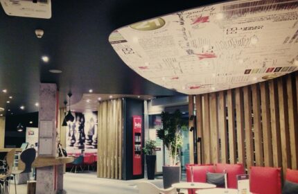 Ibis Hotel Koeln Centrum interior. Gay-friendly hotel with modern design, red seating, and unique ceiling. A comfortable space for gay travelers.