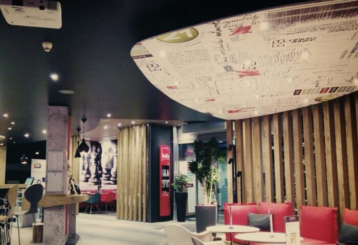 Ibis Hotel Koeln Centrum interior. Gay-friendly hotel with modern design, red seating, and unique ceiling. A comfortable space for gay travelers.