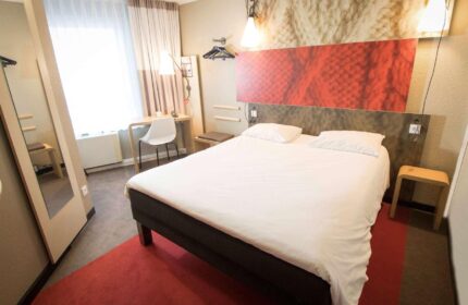Ibis Hotel Koeln Centrum room. Gay-friendly hotel with a double bed, desk, and full-length mirror. Modern design for LGBTQ+ travelers.