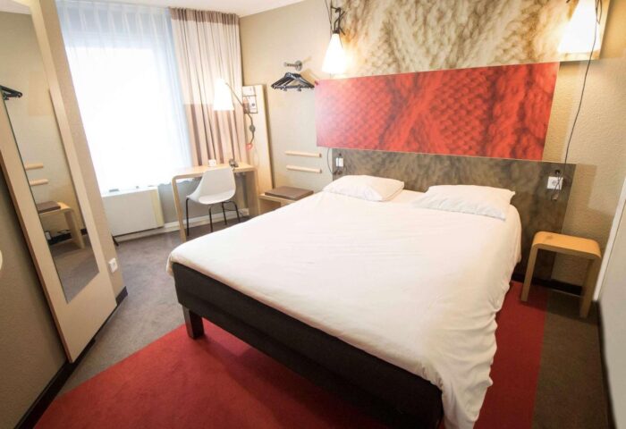 Ibis Hotel Koeln Centrum room. Gay-friendly hotel with a double bed, desk, and full-length mirror. Modern design for LGBTQ+ travelers.