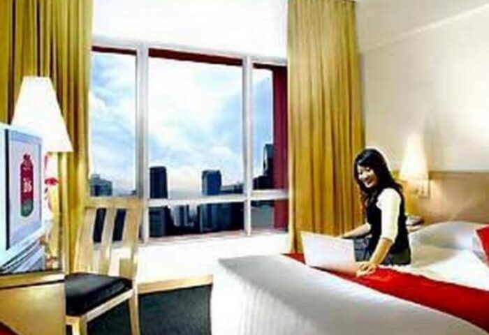 Ibis Jakarta Tamarin Hotel room: Woman with laptop, city view. Gay-friendly hotel option for travelers in Jakarta, Indonesia.
