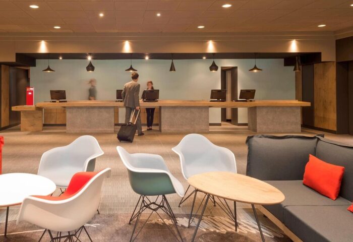 Ibis Milano Centro Hotel lobby. Gay-friendly hotel reception area with guests checking in. Modern design, comfortable seating.