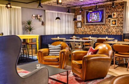 Ibis Styles London Southwark Hotel's stylish lounge area. Leather armchairs, tables, and a brick wall create a welcoming atmosphere. Gay-friendly.