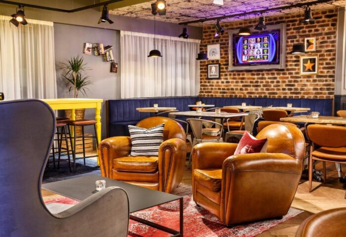 Ibis Styles London Southwark Hotel's stylish lounge area. Leather armchairs, tables, and a brick wall create a welcoming atmosphere. Gay-friendly.