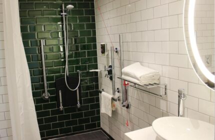 Ibis Styles London Southwark Hotel bathroom. Accessible shower with seat, grab bars, and white and green tiling. Gay-friendly hotel.