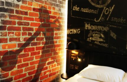 Ibis Styles London Southwark Hotel room. Brick wall with bowler hat shadow, headboard art. Gay-friendly hotel room interior design.