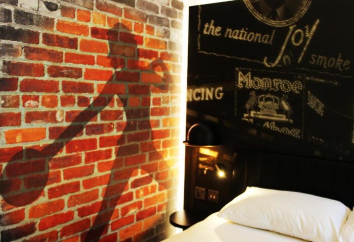 Ibis Styles London Southwark Hotel room. Brick wall with bowler hat shadow, headboard art. Gay-friendly hotel room interior design.