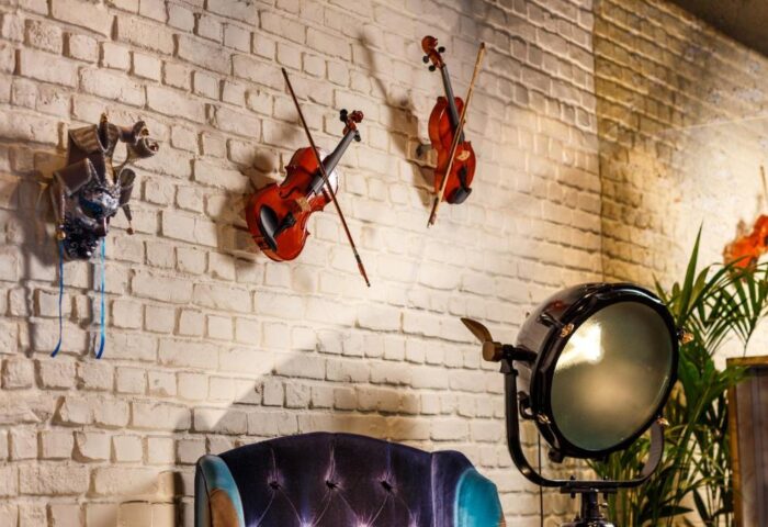 Ibis Styles London Southwark Hotel decor: violins, a mask, and a stage light adorn a brick wall. Gay-friendly hotel interior design.