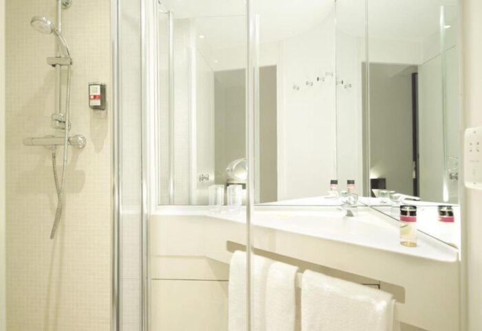 Ibis Styles London Southwark Hotel bathroom. Shower, sink, mirror, and towels in a modern, clean design. Gay-friendly hotel room detail.