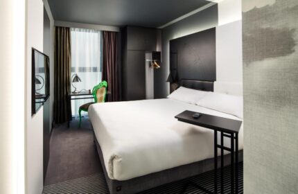 Ibis Styles London Southwark Hotel room. Modern design, white bed, desk, and green chair. Gay-friendly hotel for gay men travelers.