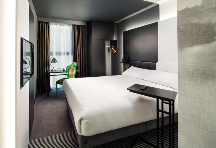 Ibis Styles London Southwark Hotel room. Modern design, white bed, desk, and green chair. Gay-friendly hotel for gay men travelers.