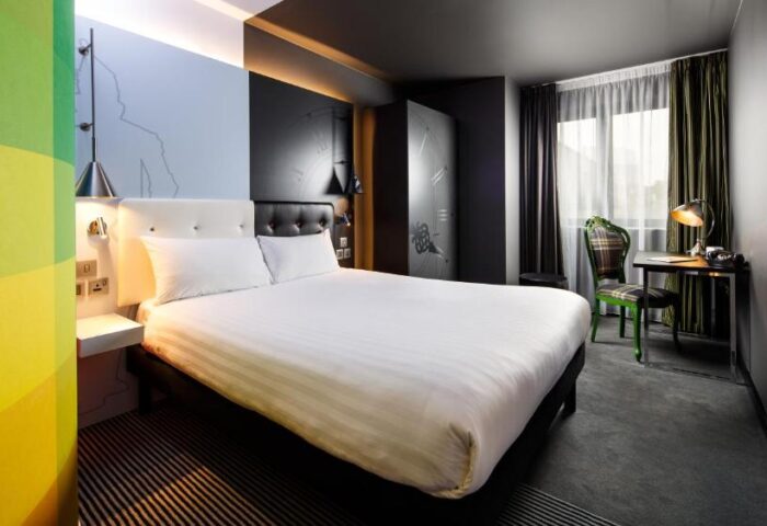 Ibis Styles London Southwark Hotel room. Gay-friendly hotel with a double bed, desk, chair, and TV. Modern design and colorful accents.