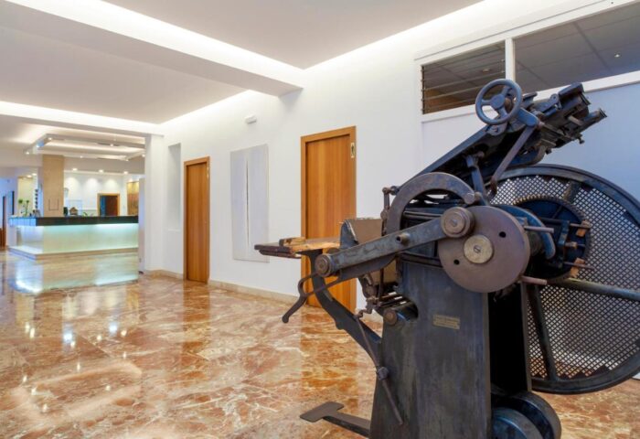 Gay-Friendly Hotel Ibiza Playa: Lobby view with vintage printing press. Marble floors, clean design. Ideal for gay travel in Ibiza.