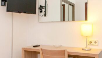 Gay-friendly hotel Ibiza Playa room featuring a desk, chair, lamp, mirror, and TV. Ideal for gay men traveling to Ibiza, Spain.