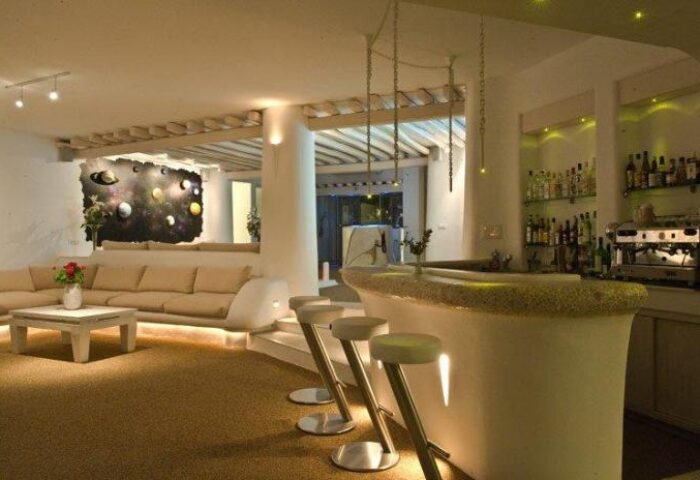 Ilio Maris Gay-Friendly Hotel bar area. Modern design with white bar stools, a cozy couch, and a cosmic mural. Ideal for gay men travel.