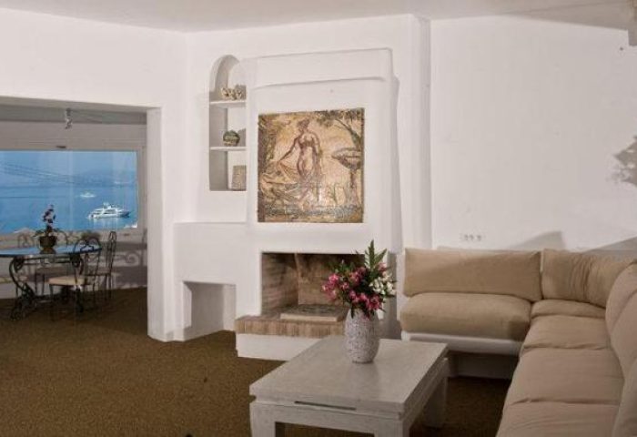 Ilio Maris gay-friendly hotel suite. Living area with couch, fireplace, and sea view. Ideal for gay men's travel, offering comfort and style.