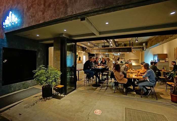 Imano Tokyo Hostel's gay-friendly hotel entrance. People at tables inside. A welcoming space for LGBTQ+ travelers. Tokyo travel advice.