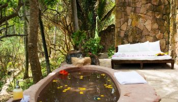 Gay-friendly Imanta Resorts Punta De Mita: Outdoor stone bathtub with flowers, daybed, and stone wall. A tranquil gay travel getaway.