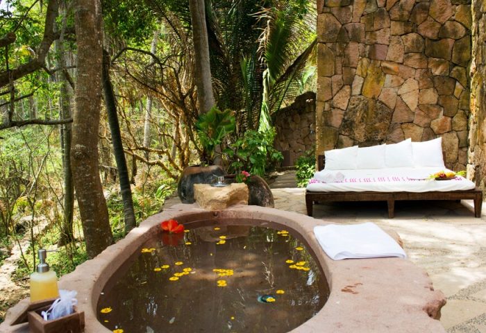 Gay-friendly Imanta Resorts Punta De Mita: Outdoor stone bathtub with flowers, daybed, and stone wall. A tranquil gay travel getaway.