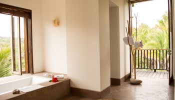Bathroom at Imanta Resorts Punta De Mita, a gay-friendly hotel. Bathtub, open window, and balcony with lush greenery. Luxury travel.