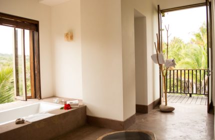 Bathroom at Imanta Resorts Punta De Mita, a gay-friendly hotel. Bathtub, open window, and balcony with lush greenery. Luxury travel.