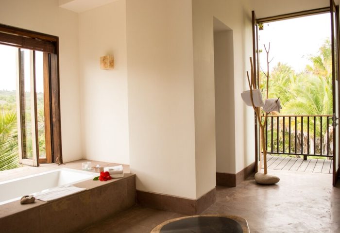 Bathroom at Imanta Resorts Punta De Mita, a gay-friendly hotel. Bathtub, open window, and balcony with lush greenery. Luxury travel.
