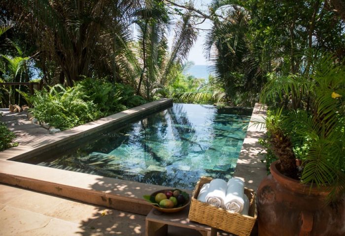 Pool at Imanta Resorts Punta De Mita, a gay-friendly hotel. Lush greenery surrounds the pool. Towels and fruit are nearby. Ocean view.