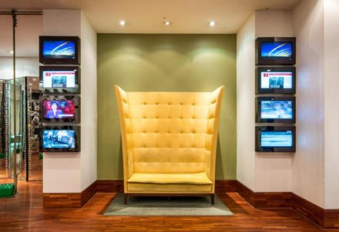Imperial Palace Boutique Hotel's unique lobby area. Yellow high-back chair and wall-mounted TVs. Gay-friendly hotel interior design.