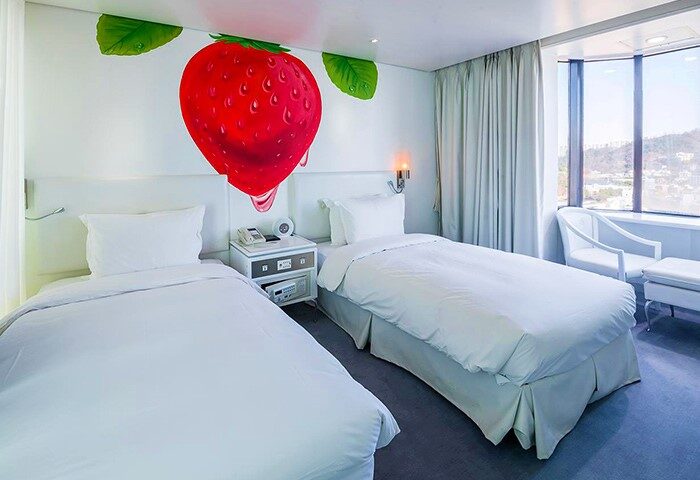 Imperial Palace Boutique Hotel room with twin beds, strawberry wall art, and city view. A gay-friendly hotel for gay men travelers.