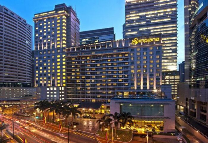 Impiana KLCC Hotel exterior at dusk. Gay-friendly hotel in Kuala Lumpur, Malaysia, with palm trees and city lights. Luxury travel destination.