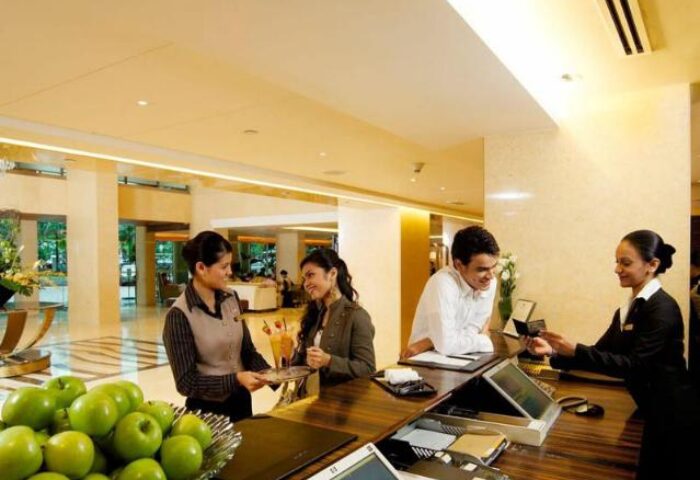 Impiana KLCC Hotel's reception area. Guests checking in, staff assisting. Gay-friendly hotel with welcoming service. Apples on the counter.