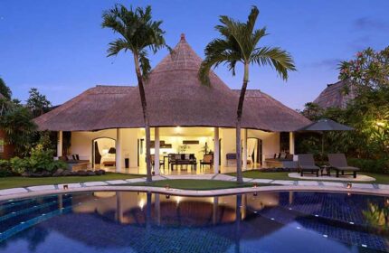 Impiana Private Villas Seminyak, a gay-friendly hotel. Pool view of villa with thatched roof, palm trees. Luxury Bali travel for gay men.