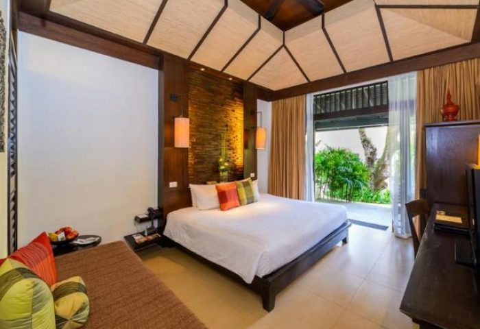 Impiana Resort Patong room. Gay-friendly hotel with a bed, daybed, and balcony. Tropical decor, wood accents, and natural light. Relaxing space.
