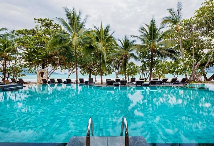 Impiana Resort Patong pool view. Gay-friendly hotel with beach access, palm trees, and lounge chairs. Ideal for gay travel in Patong, Thailand.