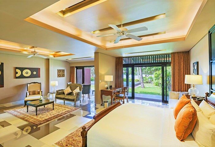 Impiana Resort Patong gay-friendly hotel room. Luxury suite with bed, seating area, desk, and balcony overlooking a tropical garden.