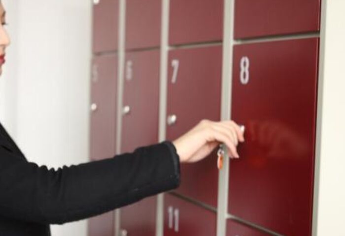 Industriepalast Hostel Berlin lockers. Gay-friendly hotel offers secure storage for travelers. Person opening red locker with key.