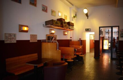 Industriepalast Hostel Berlin's gay-friendly interior. Vintage suitcases adorn the shelf above wooden booths. A unique, inviting space.