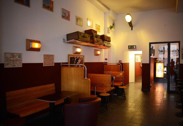 Industriepalast Hostel Berlin's gay-friendly interior. Vintage suitcases adorn the shelf above wooden booths. A unique, inviting space.