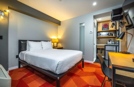 Infinity Hotel San Francisco, a Gay-Friendly Tapestry Collection by Hilton. Hotel room with bed, desk, kitchenette, and orange geometric carpet.