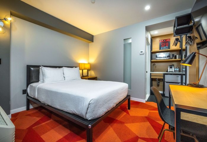 Infinity Hotel San Francisco, a Gay-Friendly Tapestry Collection by Hilton. Hotel room with bed, desk, kitchenette, and orange geometric carpet.